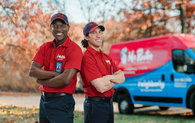 Two Mr. Rooter professionals standing back to back beside a branded van.