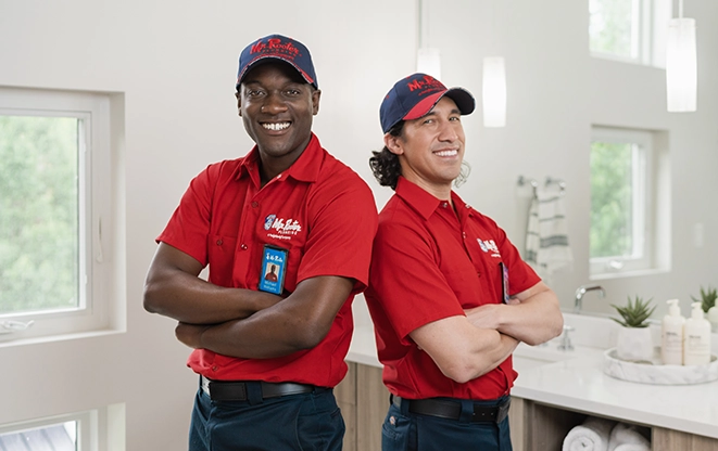 Two Mr. Rooter professionals standing back to back in a modern bathroom.