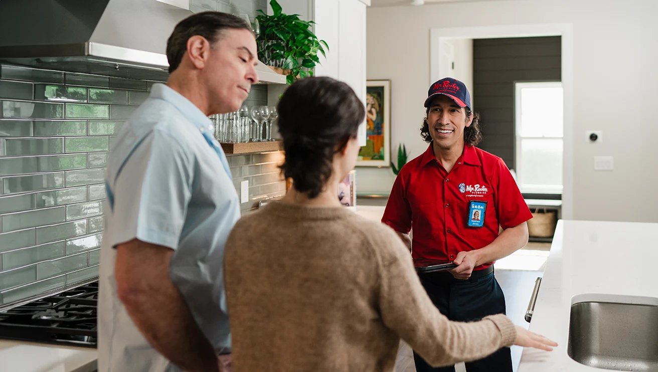 Mr. Rooter technician speaking with two customers in their kitchen.