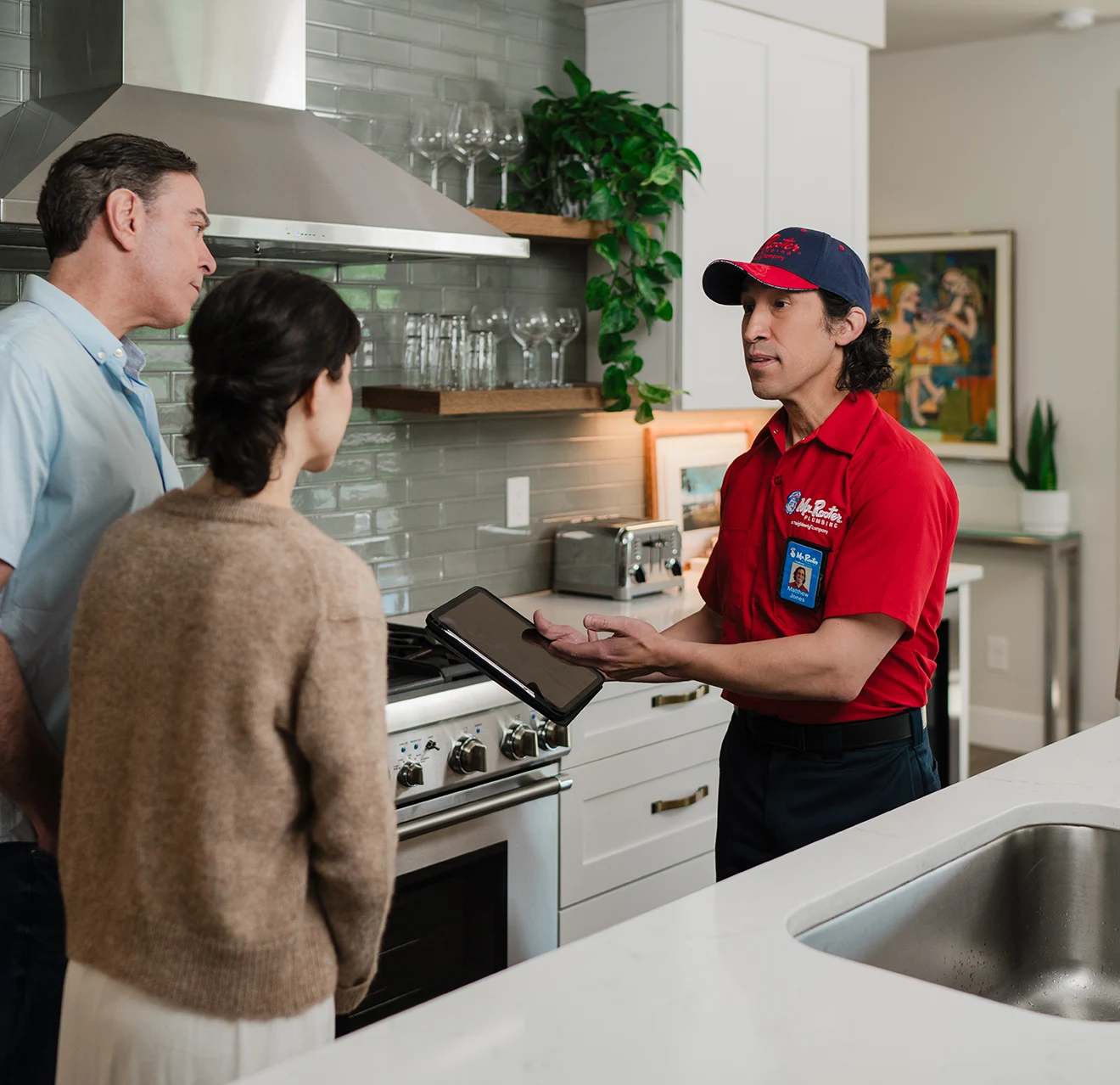 Mr. Rooter technician explaining a service plan to customers in their kitchen.