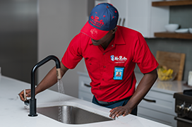 Mr. Rooter technician fixing a faucet on a kitchen sink.