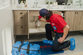 Mr. Rooter professional fixing a pipe under a sink cabinet.