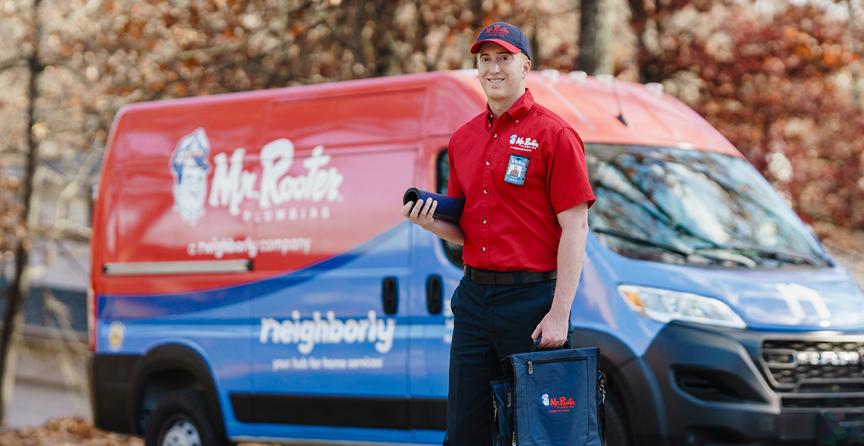 Mr. Rooter technician standing beside a branded work van.