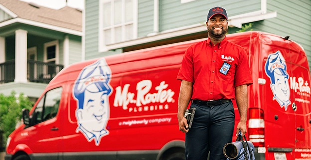 Smiling Mr. Rooter technician standing in front of a branded van.