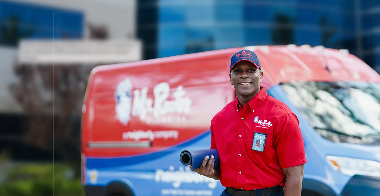 Mr. Rooter Plumbing technician standing beside a branded work van.