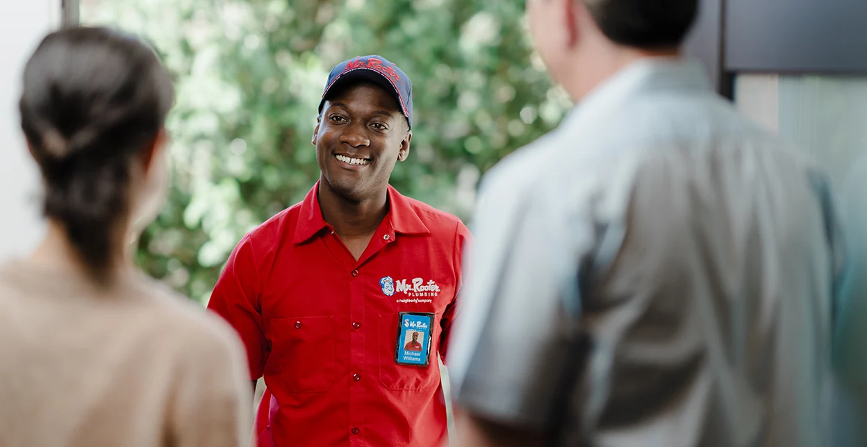 Two customers greeting a Mr. Rooter technician at their front door.