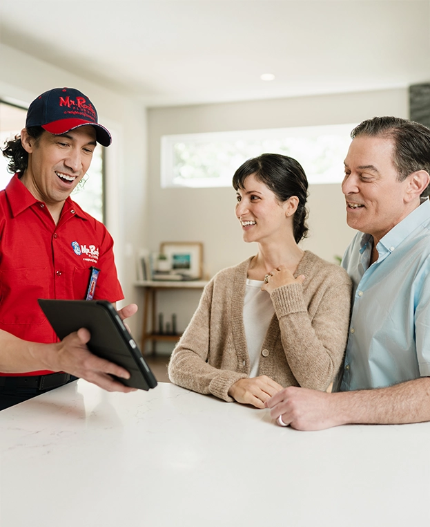 Mr. Rooter Plumbing technician going over service plan with two customers on a tablet.