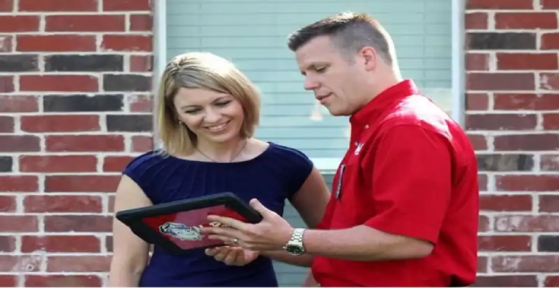 Mr. Rooter plumber with homeowner in front of brick wall, showing homeowner something on a tablet.