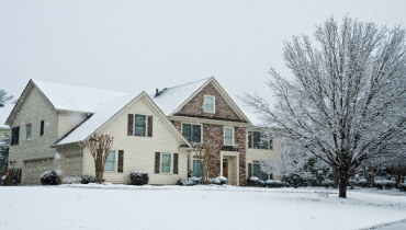 Residential home with stone front in a wintery day with snow on the lawn.