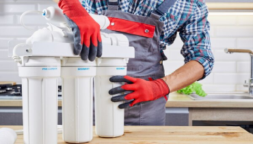 A plumber holding the filtration tanks used by common reverse osmosis systems in Calgary.