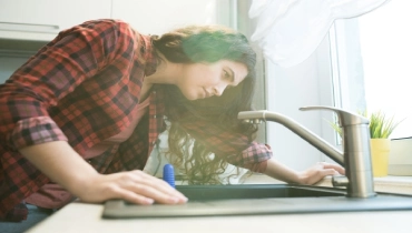 Young woman with concerned look checking kitchen faucet