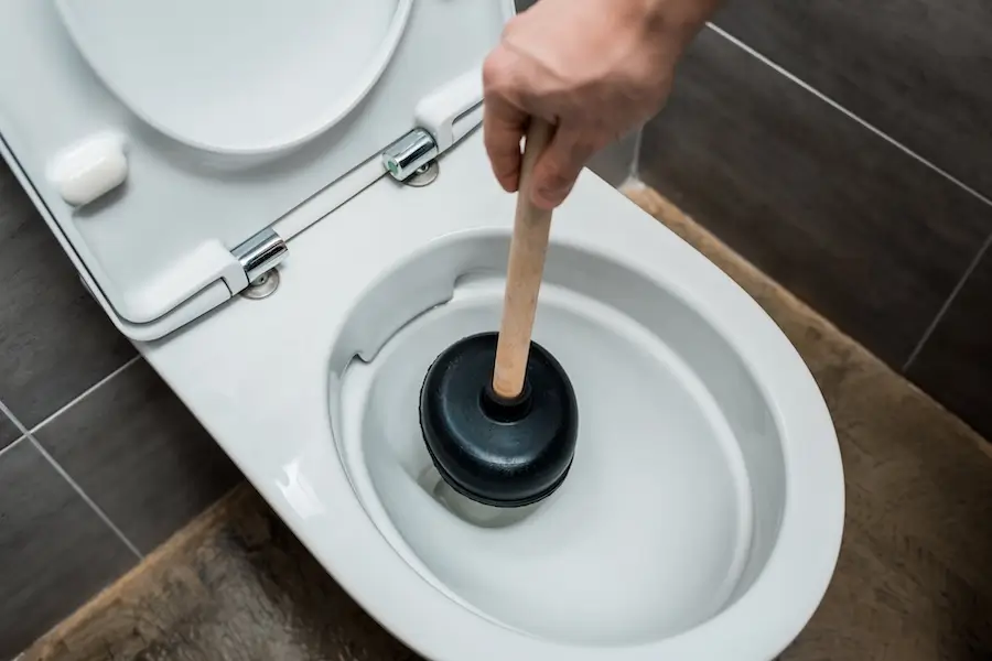A person tries to clear a toilet clog using a toilet plunger. 