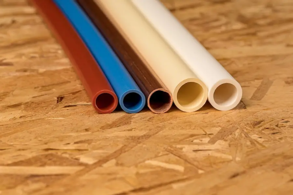  Close-up of five different types of plumbing pipes, including PEX, copper, and PVC, on a wood surface.