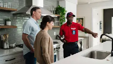 Mr. Rooter professional describing a service to two customers in their kitchen.